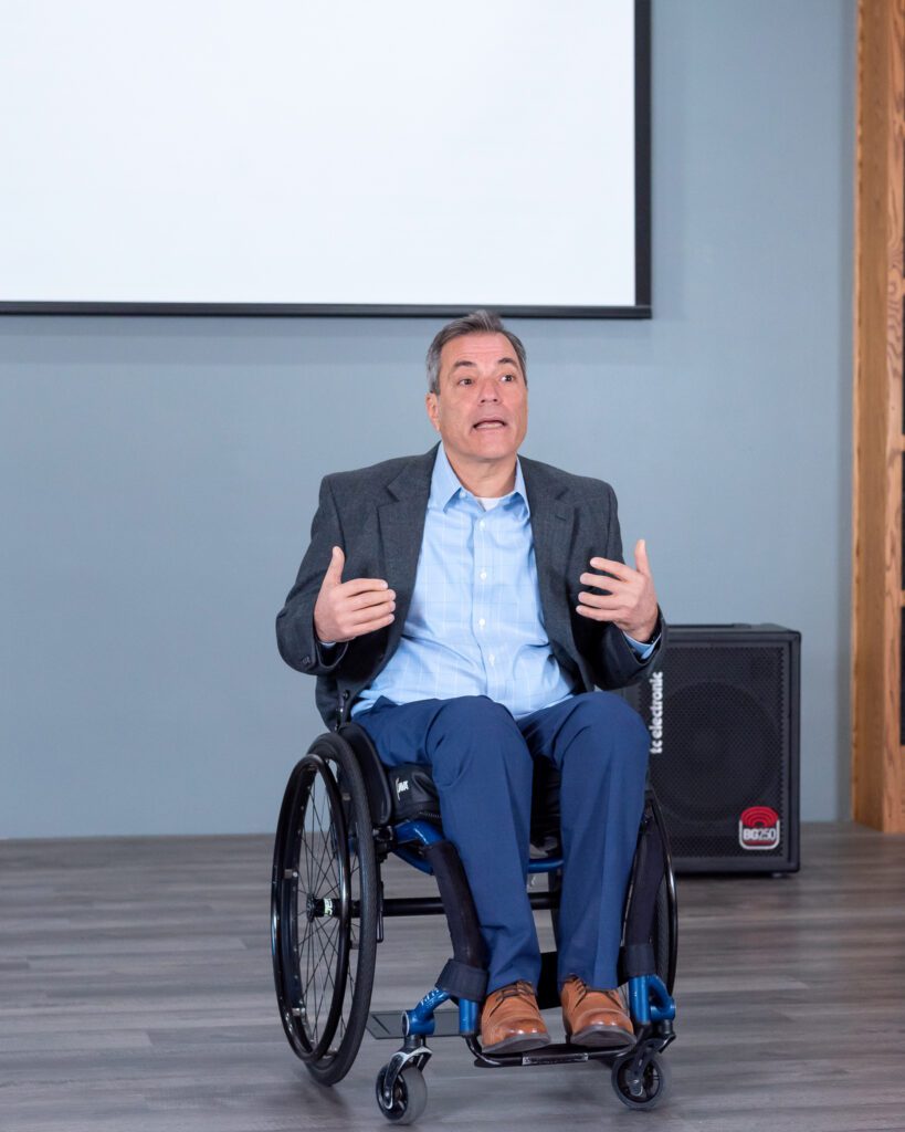 A male public speaker in a wheel chair talking on the stage.
