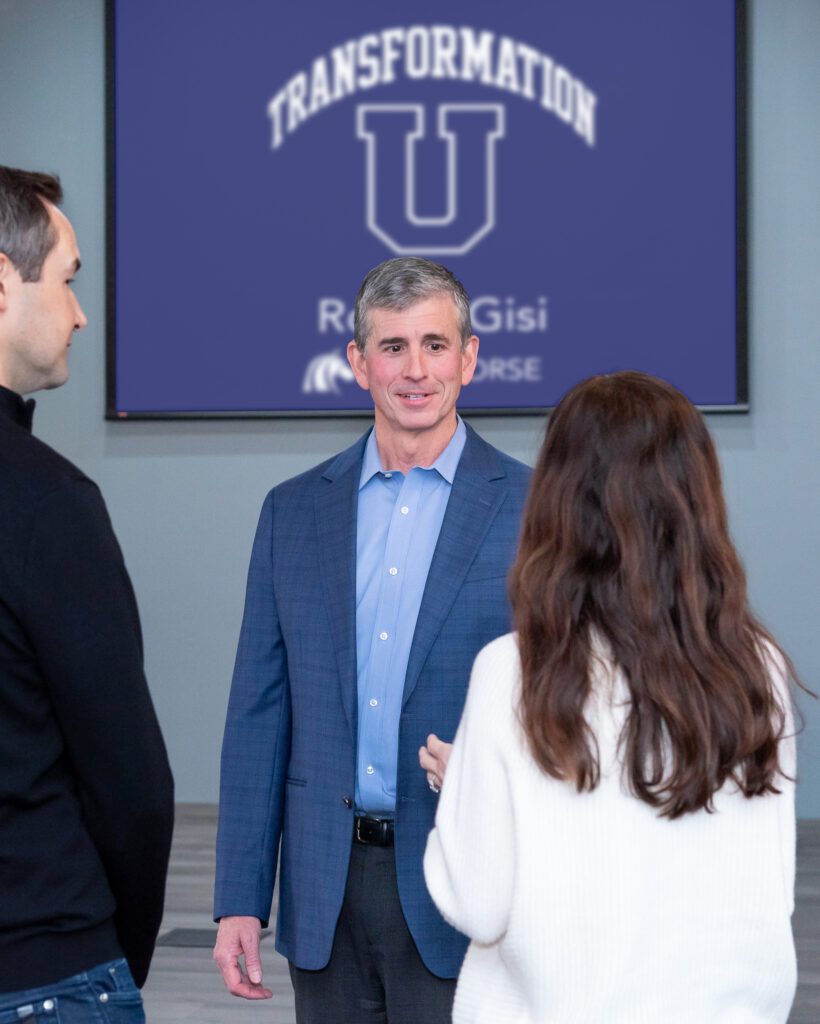 A male sports management expert talking to a female and male attendees at an event.