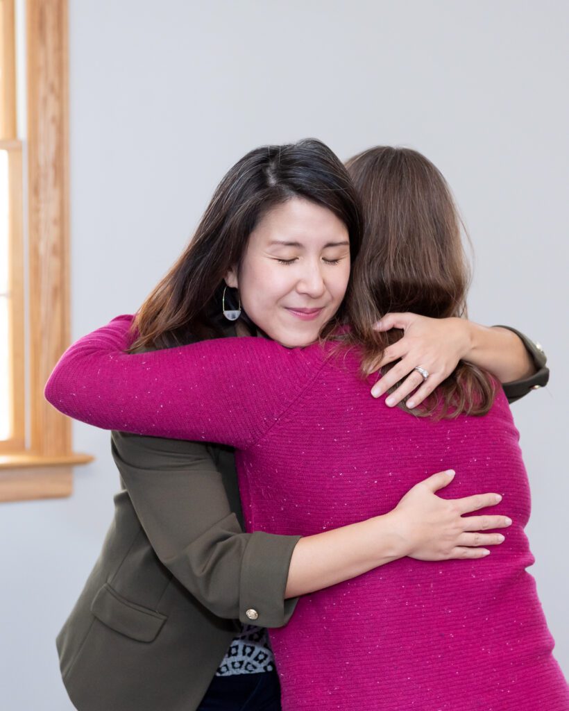 A female Asian executive coach & advisor hugging her client after a coaching session.