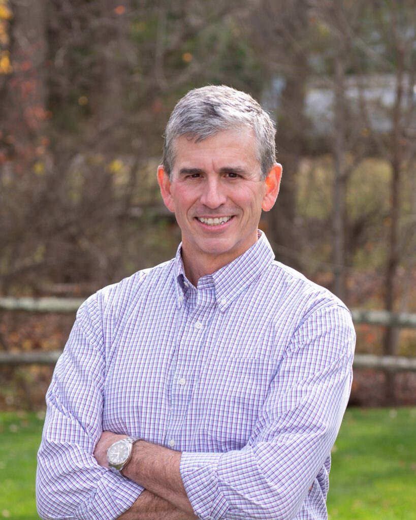 A male public speaker smiling with his arm crossed for an outdoor headshot session.