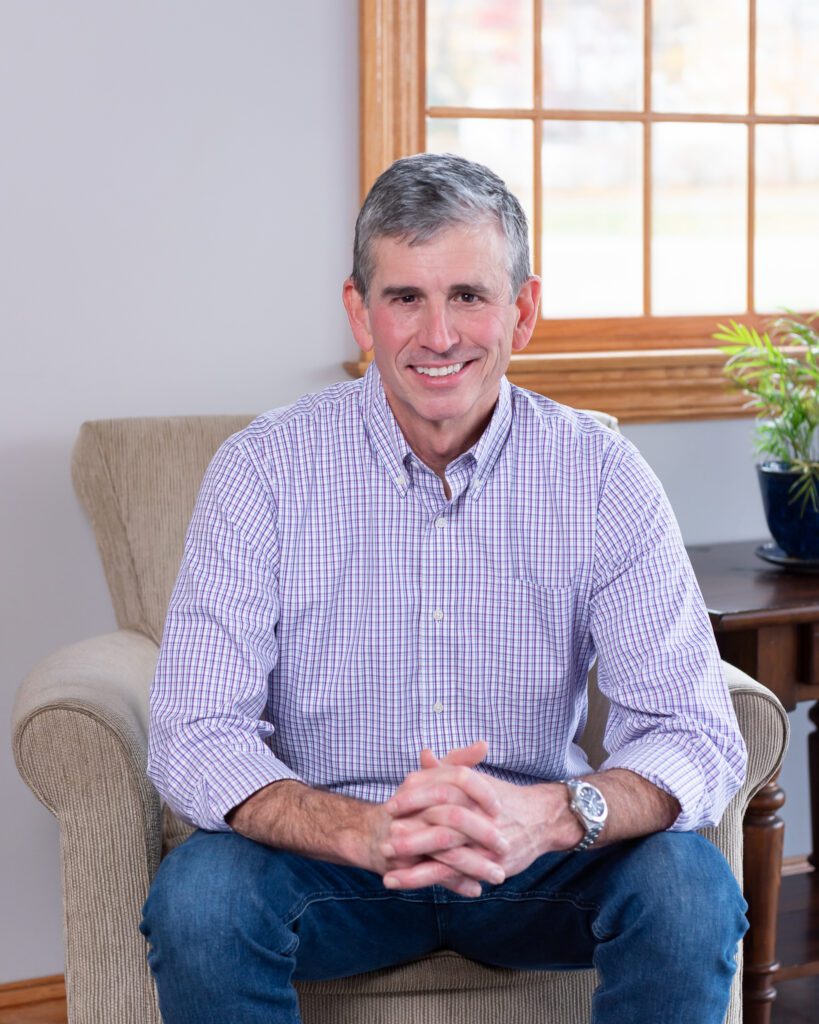 A male public speaker smiling and sitting on a couch.