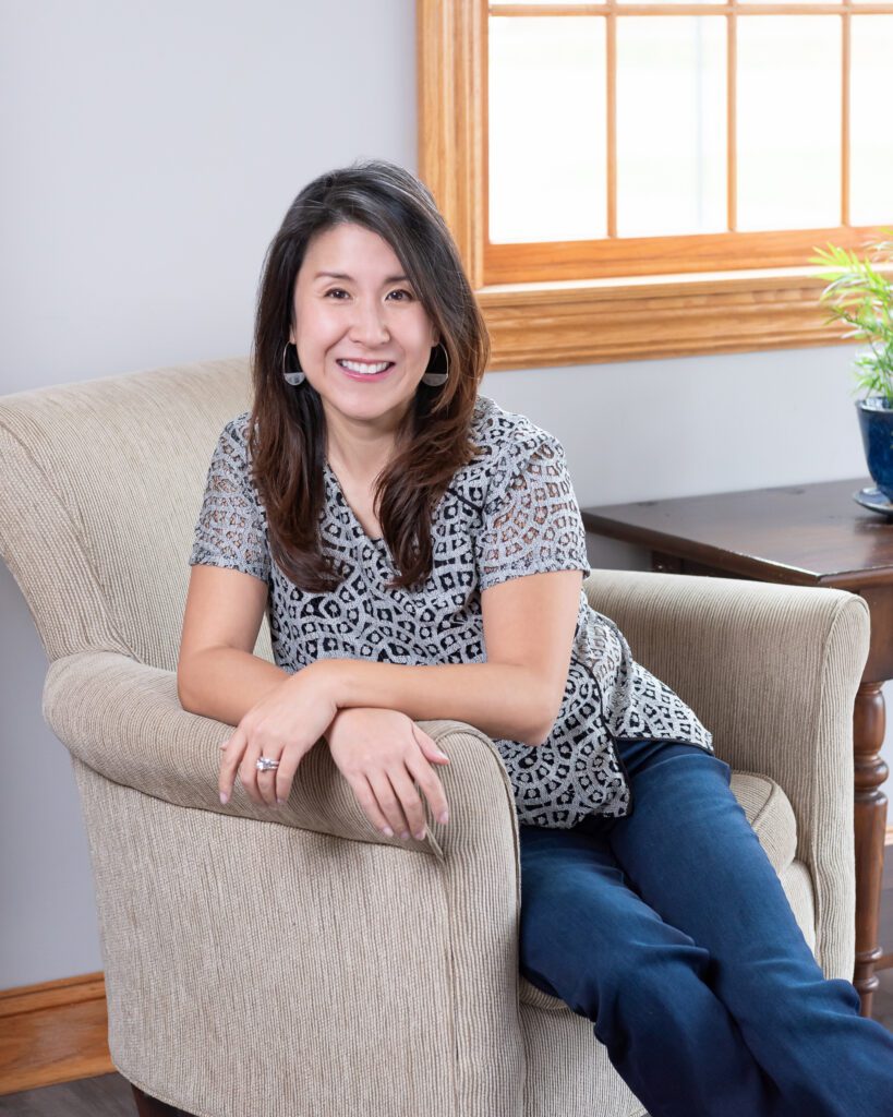 A female Asian executive coach & advisor smiling and sitting on a couch for her indoor lifestyle headshots.