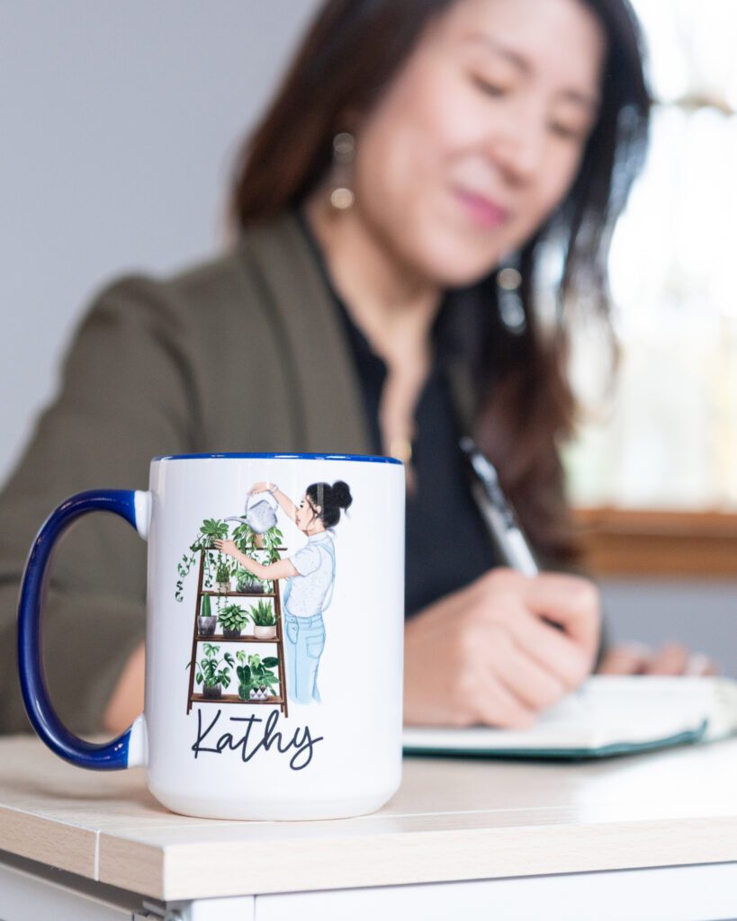 A female Asian executive coach & advisor writing in her notebook in her office with her plant-lover mug with "Kathy" on it.