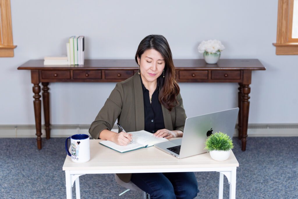 A female Asian executive coach & advisor writing in her notebook in her office.