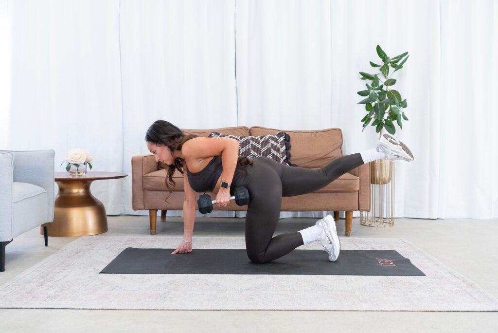 A female fitness trainer exercising with weights in her living room.