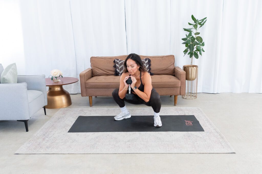 A female fitness trainer exercising with weights in her living room.