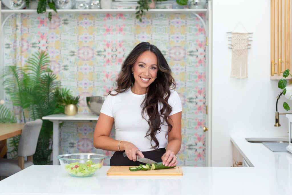 A female fitness trainer and nutrition coach preparing a bowl of salad in her kitchen.