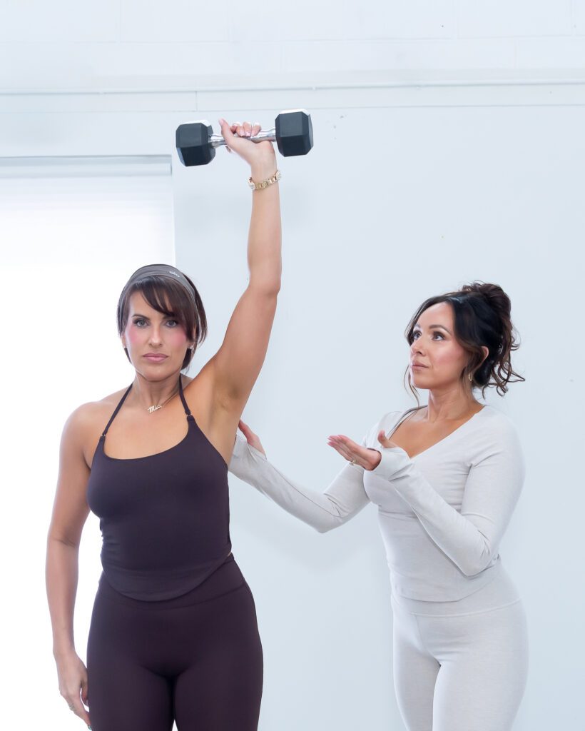 A female fitness trainer assisting her student during a weight lift exercise.