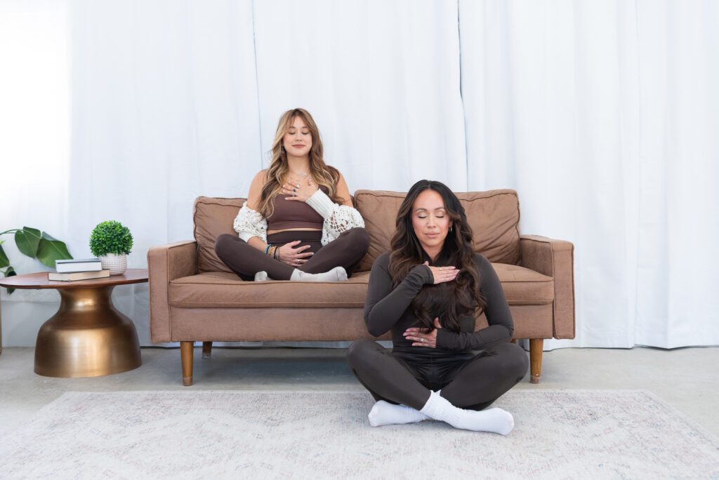 Two female fitness trainers meditating in a living room for their branding photoshoot.