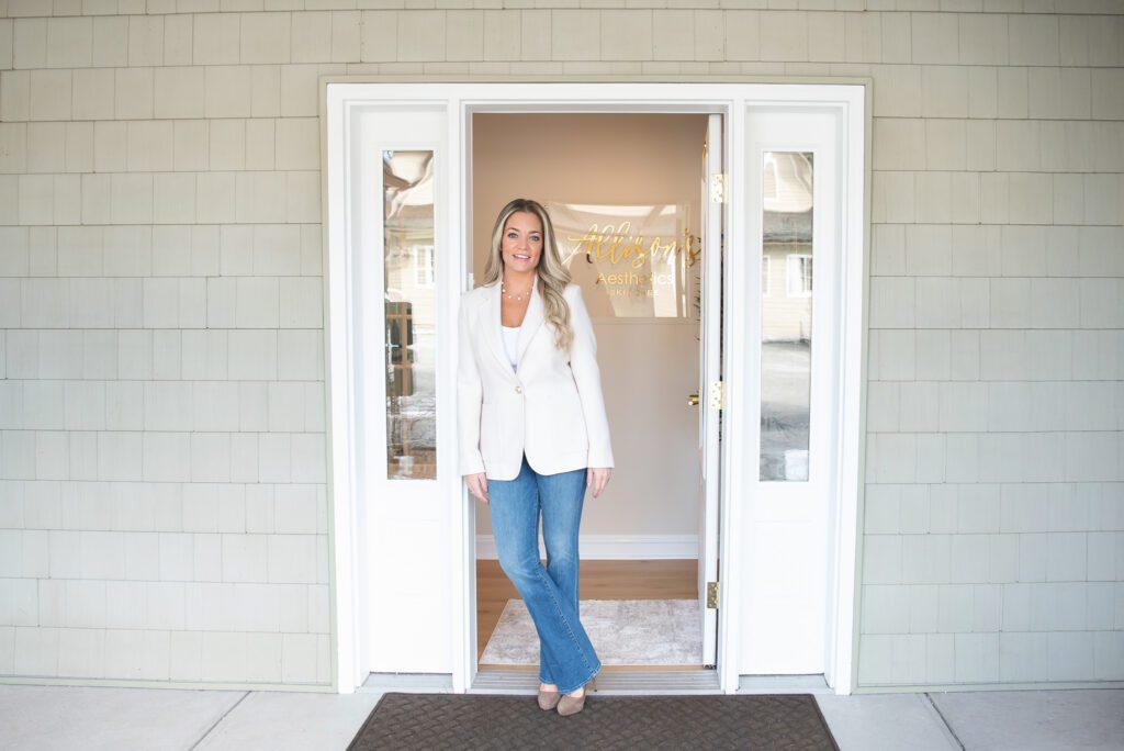 A female aesthetician leaning and standing by her front office entrance for her branding photoshoot.