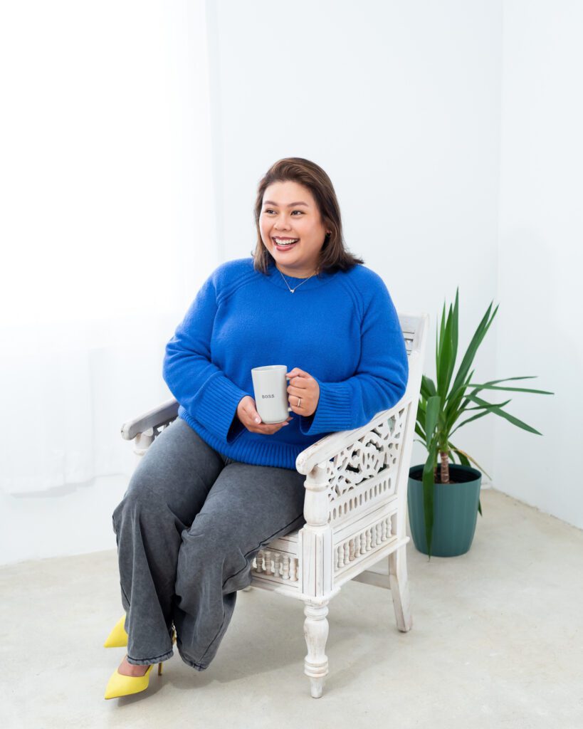 A female photo magnets creator in a blue sweater sitting and holding a mug with the word "Boss" and posing for her branding photo session.